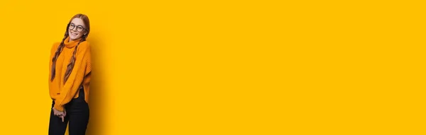 Μονόχρωμη φωτογραφία μιας κοκκινομάλλας με φακίδες και γυαλιά που χαμογελά σε έναν κίτρινο τοίχο στούντιο με ελεύθερο χώρο — Φωτογραφία Αρχείου
