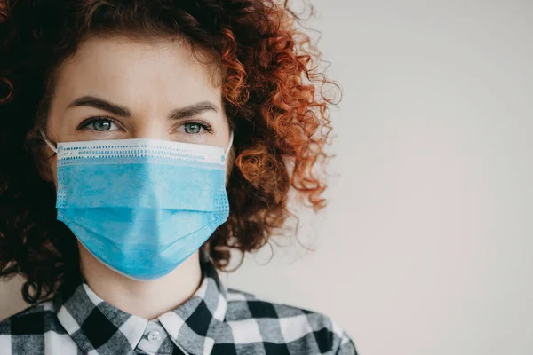 Junge Frau mit lockigem Haar trägt eine medizinische Maske auf weißem Studiohintergrund mit freiem Platz — Stockfoto