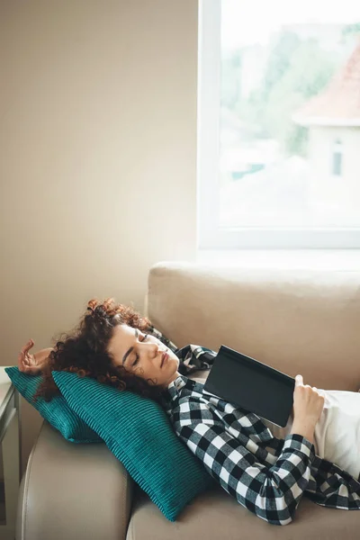 Mujer caucásica soñolienta con el pelo rizado descansando en el sofá después de leer un libro — Foto de Stock