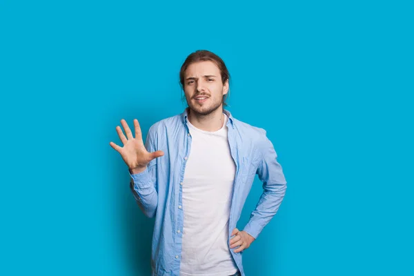 Homem caucasiano com cabelos longos e barba gesticulando número 5 com palma enquanto posando em uma parede azul estúdio — Fotografia de Stock