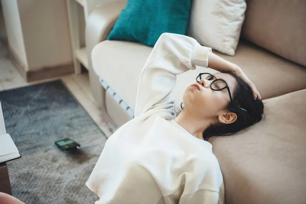 Zmęczona biała kobieta w okularach odrabiająca lekcje na podłodze i słuchająca muzyki ze słuchawek — Zdjęcie stockowe