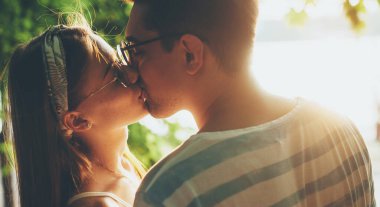 Parkta eğlence ışığında gözlük takan ve öpüşen sevimli bir çift.