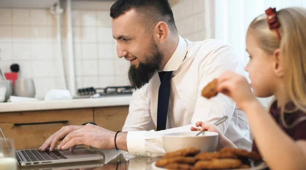 Καυκάσιος επιχειρηματίας με γενειάδα που δουλεύει στον υπολογιστή και η κόρη του τρώει μπισκότα στο ίδιο τραπέζι — Φωτογραφία Αρχείου
