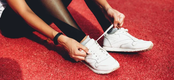 Close up foto de uma menina caucasiana fixando seus sapatos esportivos antes de uma cruz em um estádio vermelho — Fotografia de Stock