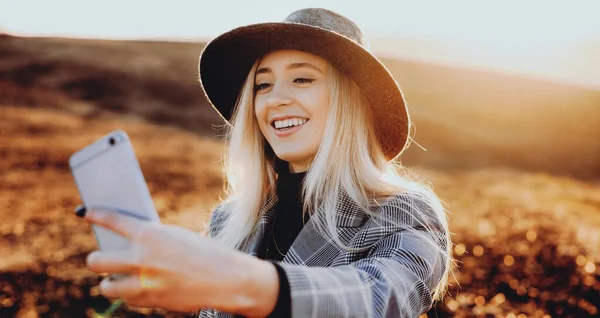 Wunderschöne blonde kaukasische Dame mit schönem Hut, die ein Selfie macht, während sie auf einem sonnigen Feld lächelt — Stockfoto
