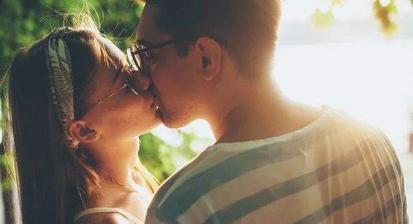 Charming couple wearing eyeglasses and kissing outside in the light of fun in a park — Stock Photo, Image