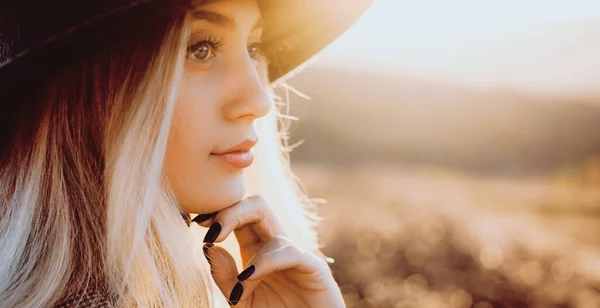 Encantadora mujer caucásica con cabello rubio y sombrero posando en un campo mirando hacia otro lado — Foto de Stock