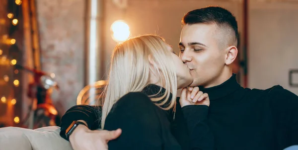 소파에 기대어 따뜻 한 분위기에서 금발의 아름다운 여자와 애인 이 거실에서 키스를 하는 모습 — 스톡 사진