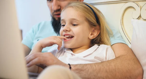 금발 소녀가 수염을 기른 아버지와 함께 소파에 누워 무언가를읽으면서 시간을 보내는 모습 — 스톡 사진