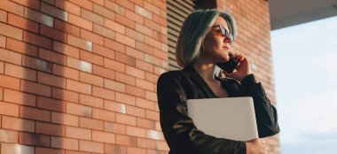 Kafkasyalı iş adamı, elinde bir dizüstü bilgisayarla dışarıda telefonla konuşuyor.