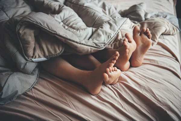 De cerca foto de los pies cubiertos por una colcha de una pareja caucásica acostada en la cama — Foto de Stock