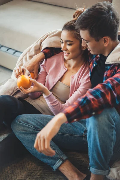 Kaukázusi pár ül a padlón, takaróval borítva és narancsot esznek, megölelve egymást. — Stock Fotó