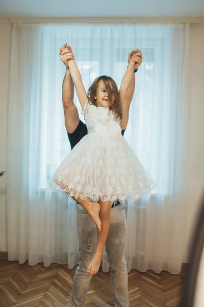 Caucásica madre sosteniendo a su hija en un vestido blanco posando como una bailarina y mirando a la cámara —  Fotos de Stock