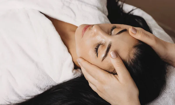 Mulher branca deitada em um centro de spa e tendo uma sessão de massagem na cabeça com os olhos fechados — Fotografia de Stock