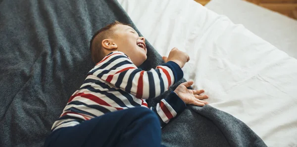 Caucásico chico riendo en el sofá jugando solo y teniendo encantadora sonrisa de la infancia —  Fotos de Stock