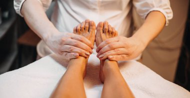 Beyaz masör, kaplıca merkezinde bir müşteriyle ayak masajı yapıyor.