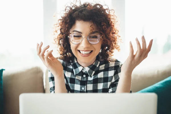 Gözlüklü ve kıvırcık saçlı mutlu bir kadın internette kameraya bakıp gülümsüyor. — Stok fotoğraf