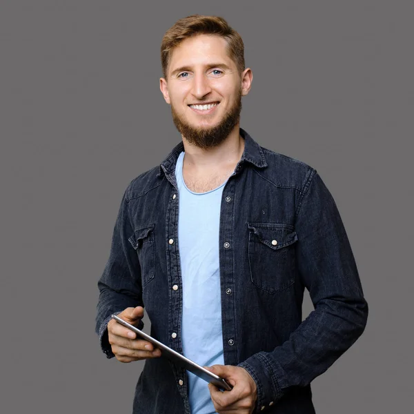 Homem caucasiano gengibre com barba segurando um tablet e promovendo serviços de TI enquanto sorri em uma parede de estúdio cinza — Fotografia de Stock