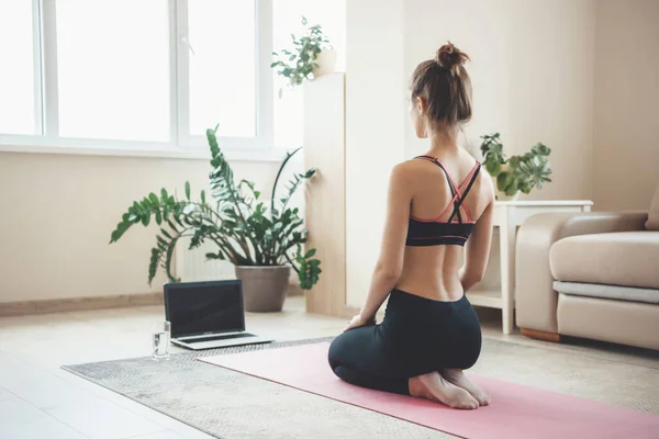 Volver ver foto de una mujer atlética caucásica en ropa deportiva meditando en frente de la computadora portátil en el suelo —  Fotos de Stock