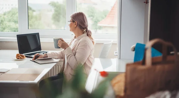 Senior caucasian woman with blonde hair working at the laptop with free space from home — Stock Photo, Image