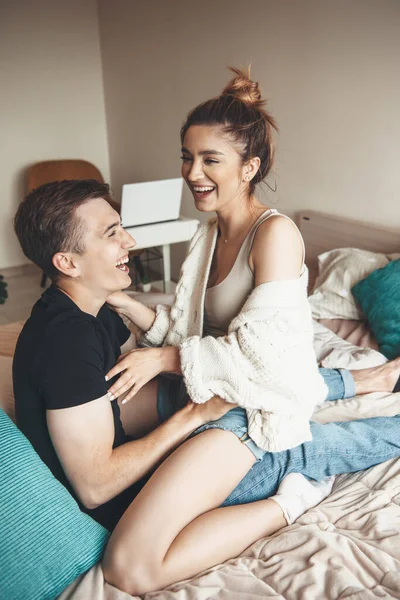 Preciosa pareja joven tumbada en la cama y abrazándose mientras sonríe en el fin de semana —  Fotos de Stock