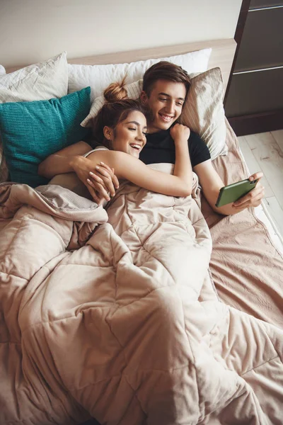 Adorável casal caucasiano deitado cama e assistindo algo no celular — Fotografia de Stock