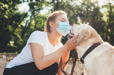 Yüzünde tıbbi maske olan sevimli sarışın kadın tecrit sırasında dışarıda köpeğiyle oynuyor.