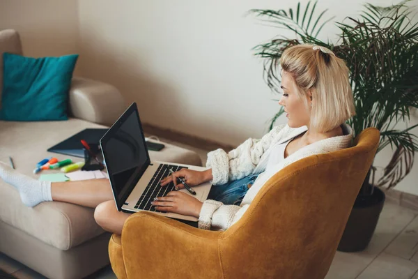 Ocupada mujer caucásica con el pelo rubio charlando en el portátil y haciendo la tarea en casa en línea — Foto de Stock