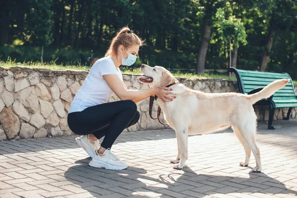 Blondynka, biała kobieta w masce przeciw grypie spędza czas na zewnątrz ze swoim psem. — Zdjęcie stockowe