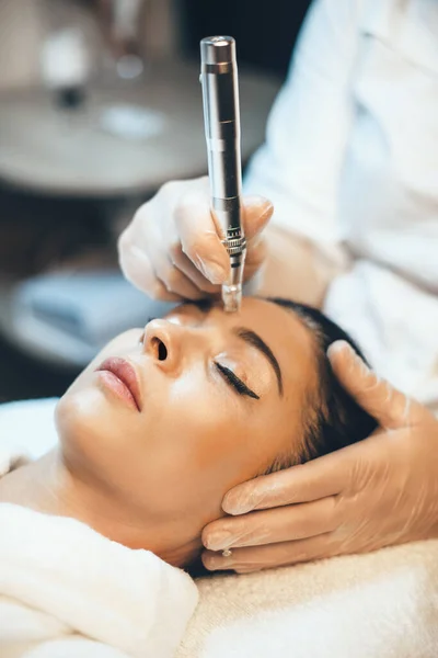 Acne treatment procedure to a brunette lady on face lying on spa couch in a wellness salon