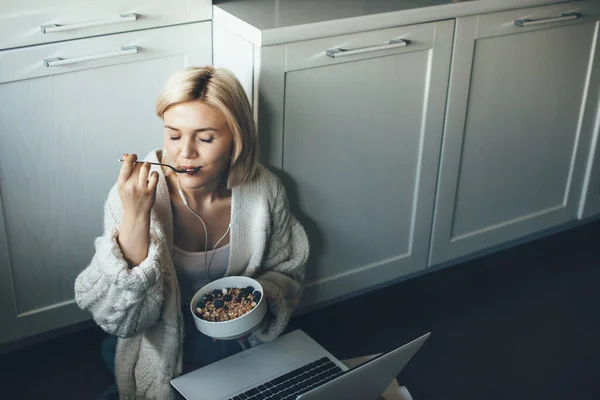 Foto vista superior de una mujer rubia a dieta comiendo cereales en el suelo mientras usa una computadora portátil — Foto de Stock