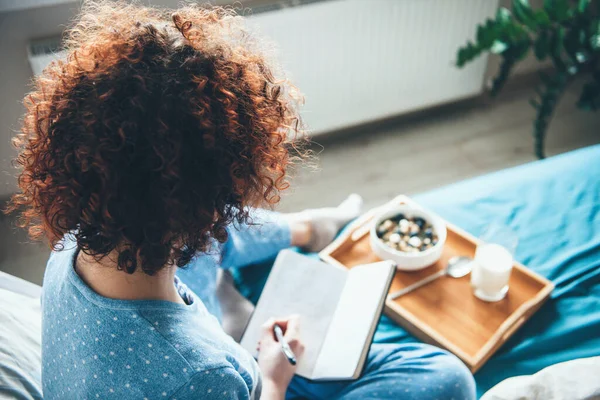 Vista superior foto de una mujer caucásica de pelo rizado con hábitos saludables leyendo un libro en la cama y comiendo cereales con leche — Foto de Stock