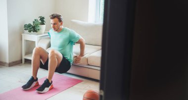 Spor giyimli sarışın beyaz adam evde fitness yapıyor.