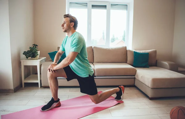 Foto laterale di un uomo sportivo che fa fitness a casa su un tappeto sportivo durante la quarantena — Foto Stock