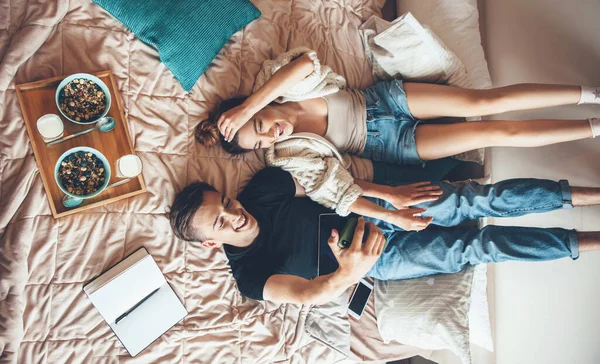 Upper view photo of a caucasian couple lying in bed and studying while eating cereals with milk — Stock Photo, Image