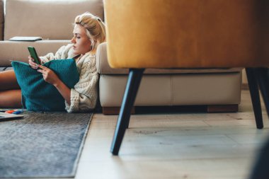 Laptopun başında çalışırken yerde telefon kullanarak örgü ören sarışın kadın.