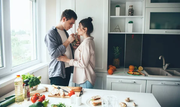 Adorável jovem casal bebendo juntos mojito enquanto prepara o jantar juntos na cozinha — Fotografia de Stock