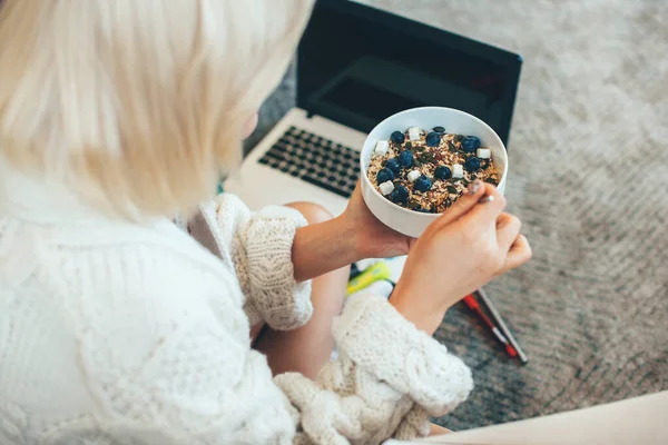 Vista superior de una mujer rubia caucásica comiendo cereales mientras trabajaba en el portátil en el suelo — Foto de Stock