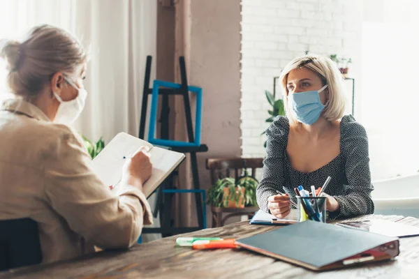 Occupato anziana donna d'affari che lavora da casa con un cliente che indossa una maschera medica sul viso e utilizzando alcuni libri e documenti — Foto Stock