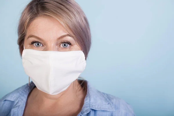 Nahaufnahme Foto einer kaukasischen Frau mit blonden Haaren, die eine medizinische Maske auf blauer Studiowand mit freiem Platz trägt — Stockfoto