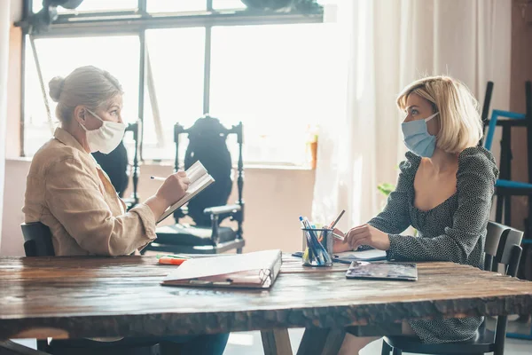 Femeie caucaziană în vârstă care lucrează cu un client acasă cu niște documente care poartă o mască medicală pe față — Fotografie, imagine de stoc