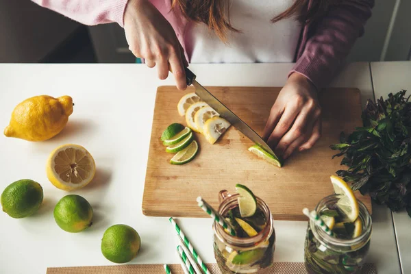 Foto vista superior de una mujer caucásica cortando frutas y haciendo una bebida mojito de limón y lima —  Fotos de Stock