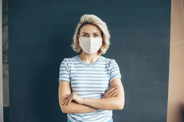 Vorderseite Foto einer kaukasischen Frau mit medizinischer Maske im Gesicht posiert mit verschränkten Armen an einer grauen Studiowand — Stockfoto