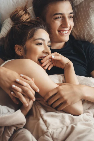 Preciosa pareja caucásica acostada en la cama y abrazándose mientras sonríe y se toma de la mano —  Fotos de Stock