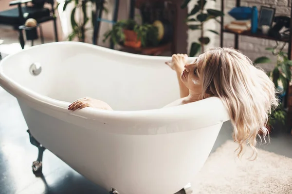 Senior caucasian woman posing in a bathtub with an anti aging cream on face — Stock Photo, Image