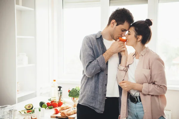 Lovely caucasian couple eating orange together in the kitchen while preparing food