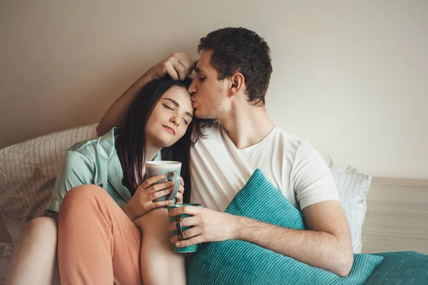 Casal encantador na cama beijando e relaxando enquanto bebe um chá pela manhã — Fotografia de Stock