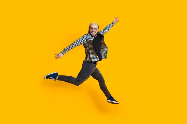 Saltando homem caucasiano com cabelo loiro e óculos está ouvindo música na parede do estúdio amarelo — Fotografia de Stock