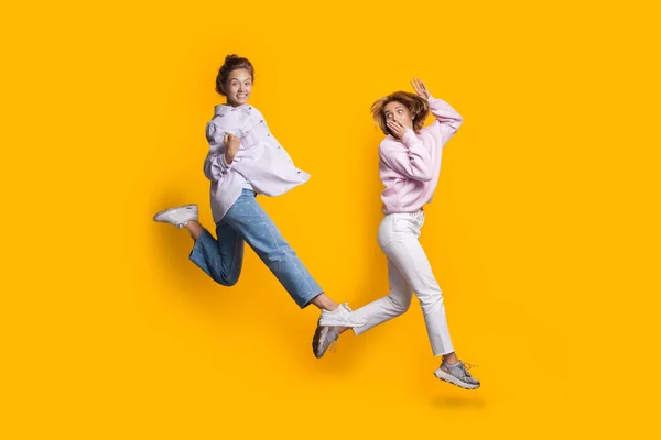 Zwei springende kaukasische Blondinen spielen und haben Spaß an der gelben Studiowand — Stockfoto