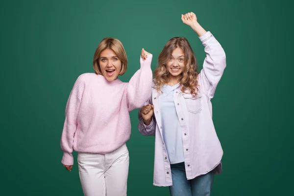 Charmante blonde Frauen posieren mit den Händen über der grünen Studiowand und lächeln in die Kamera — Stockfoto